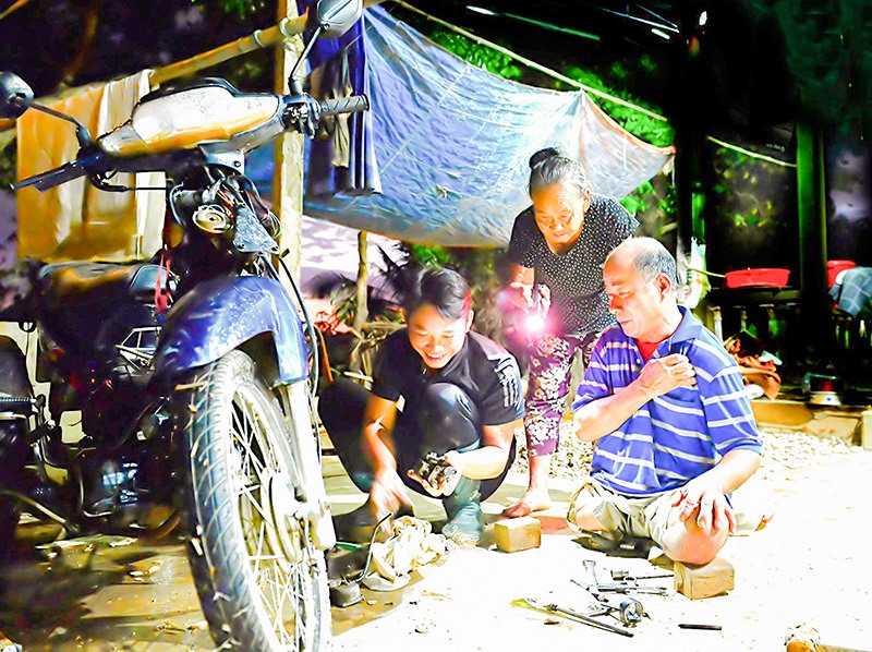 Anh Nguyễn Thanh Tuấn sửa xe giúp người dân vùng ngập lụt đến tận đêm -Ảnh: L.T​