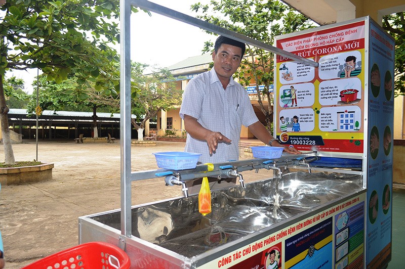Thầy giáo Hoàng Văn Ba bên sản phẩm xe bồn rửa tay di động do mình mày mò sáng chế để phục vụ việc rửa tay cho học sinh Ảnh: Đ.V