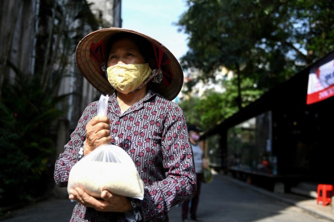 Một phụ nữ đeo khẩu trang nhận túi gạo miễn phí tại một góc phố cổ Hà Nội hôm 27/4/2020 (Ảnh: AFP/ Nhac Nguyen).