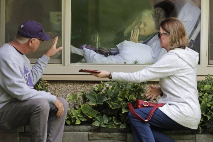 Judie Shape (ở giữa) người nhiễm Covid-10 đang chào những người con của mình qua cửa kính. Ảnh: AP