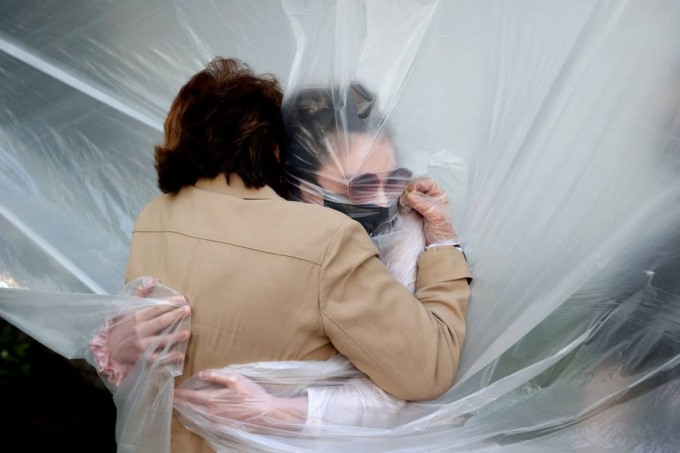 Olivia Grant ôm bà của mình, Mary Grace Sileo, qua một tấm vải nhựa ở Wantagh, New York ngày 24/5. Ảnh: Getty Images