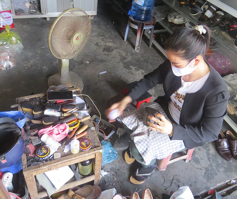 Chị Lê Thị Trang tỉ mẩn với việc sửa giày, dép cũ nơi góc phố -Ảnh: KHÁNH LINH