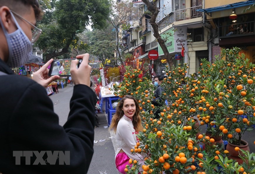 Du khách nước ngoài trong trang phục áo dài Việt Nam thích thú chụp ảnh tại chợ hoa Hàng Lược. (Ảnh: Hoàng Hiếu/TTXVN)