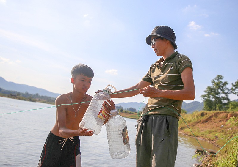 Thầy giáo Phan Hoàng Bách buộc bon nhựa làm dãy phao cảnh báo trên sông Đakrông cho trẻ em tập bơi-Ảnh: LÊ TRƯỜNG