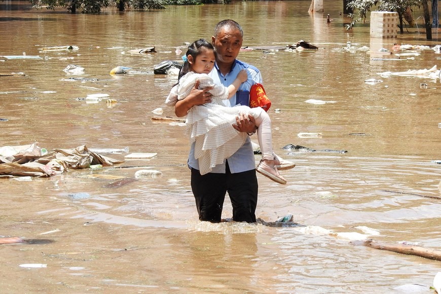 Sơ tán trẻ em khỏi khu vực bị ngập do mưa lũ. (Ảnh: AFP/TTXVN)