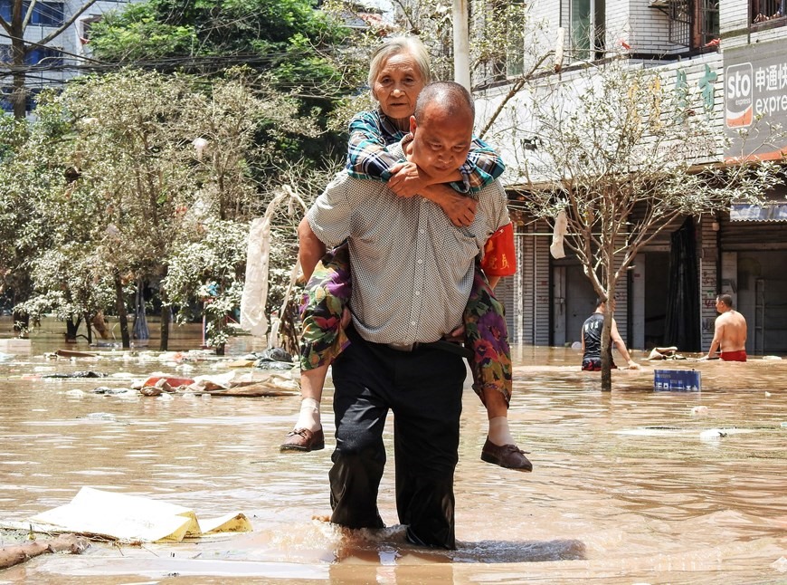 Sơ tán người già khỏi khu vực bị ngập do mưa lũ. (Ảnh: AFP/TTXVN)