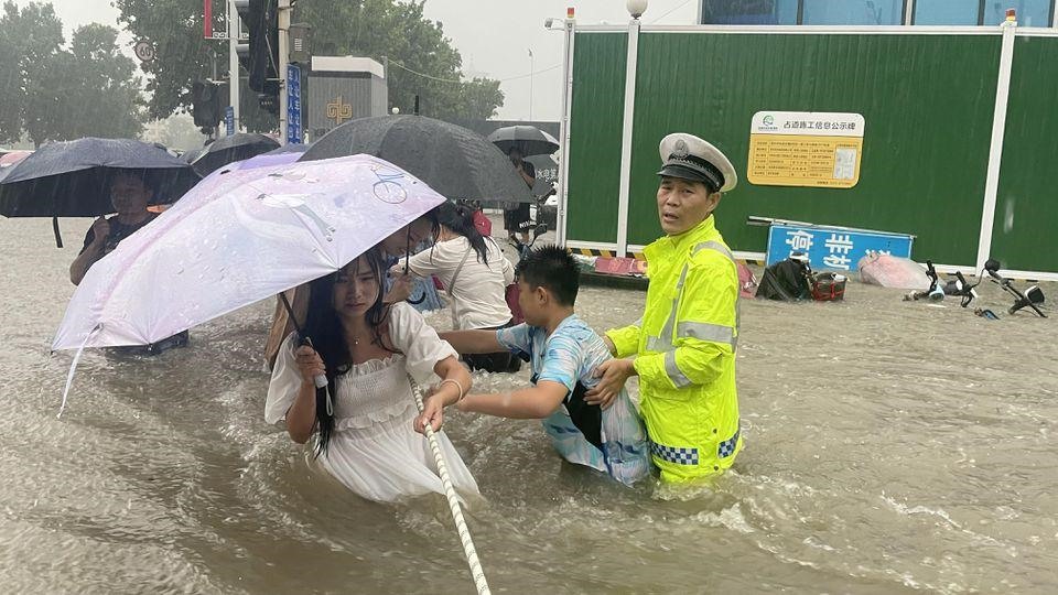 Người dân Trịnh Châu bám vào dây thừng để băng qua dòng nước lũ. Ảnh: Reuters