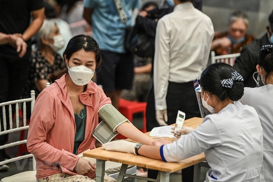 Người dân được nhân viên y tế tư vấn sức khỏe, kiểm tra huyết áp và thân nhiệt trước khi tiêm. (Ảnh: PV/Vietnam+)