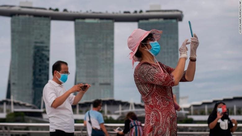 Một người phụ nữ đeo khẩu trang và đeo găng tay chụp ảnh tại Vịnh Marina của Singapore vào ngày 1/8/2021. Ảnh: CNN