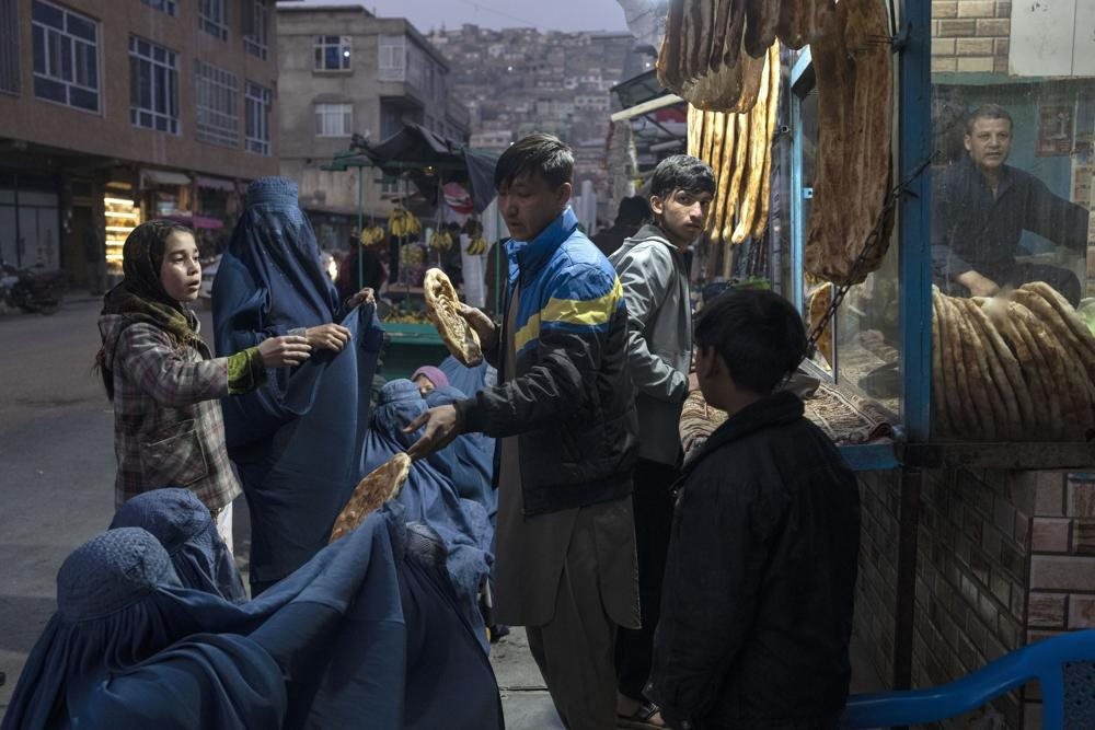 Một người đàn ông phân phát bánh mì cho những phụ nữ Afghanistan mặc áo Burka bên ngoài một tiệm bánh mì ở Kabul, Afghanistan vào ngày 2/12/2021. Ảnh: AP