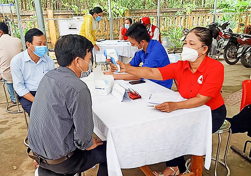 Bà Ngô Thị Đào (bên phải) hỗ trợ đo thân nhiệt cho người dân đến tiêm vắc xin COVID-19 tại Trạm Y tế xã Cam Hiếu -Ảnh: ANH VŨ