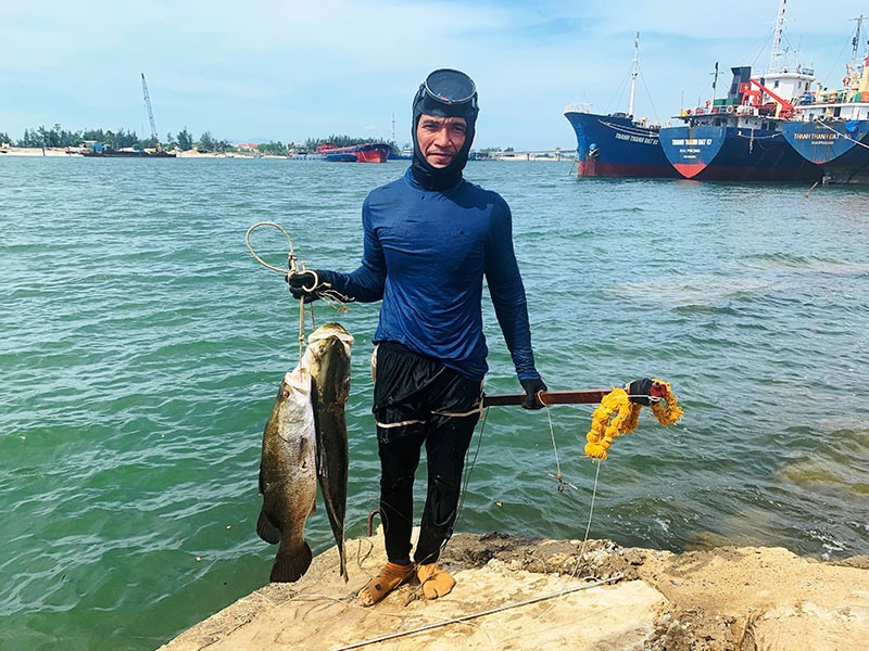 Anh Nguyễn Văn Xinh bên chiến lợi phẩm của mình là 2 con cá vược bắn được từ dưới rạn đá ở khu vực cảng Cửa Việt - Ảnh: ĐV