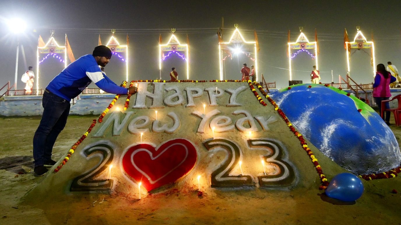 Một người đàn ông thắp nến trên hình Chúc mừng năm mới 2023 bằng cát ở Prayagraj, Ấn Độ. Ảnh: AFP/Getty Images