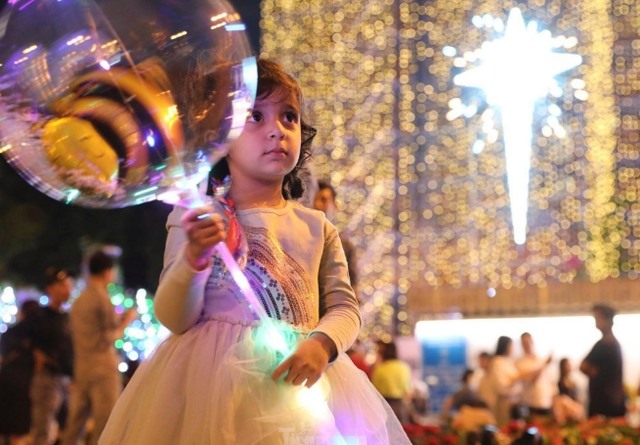Một em bé người nước ngoài xuống phố vui chơi, hòa mình vào không khí nhộn nhịp đêm Giáng sinh.
