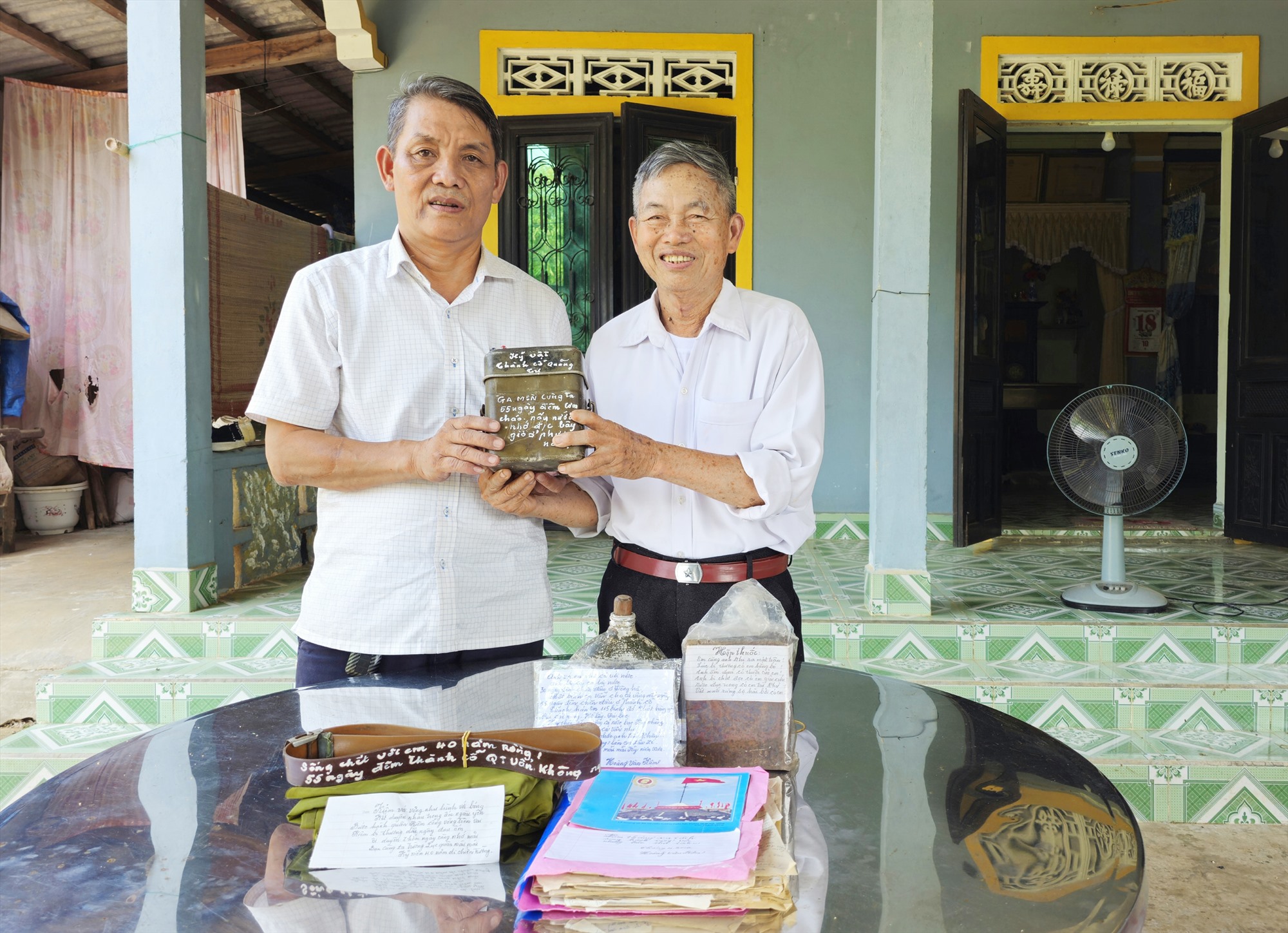 Ông Thân Trọng Dũng (bên trái), Chủ tịch UBND xã Vĩnh Sơn nhận các kỷ vật được ông Hoàng Văn Kiệm tặng -Ảnh: TÚ LINH